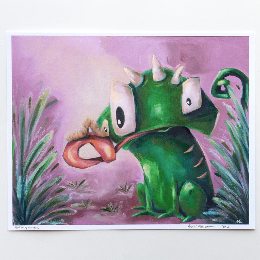 A colorful art print featuring a green cartoon lizard character with large white eyes and a long pink tongue sticking out, surrounded by stylized green plants on a pink-purple background. The print is shown against a clean white backdrop.