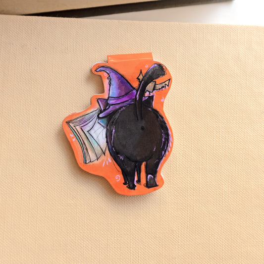 back of magnetic bookmark image of a black cat wearing a purple witches hat with a bat overhead and spellbook hovering in front of it.