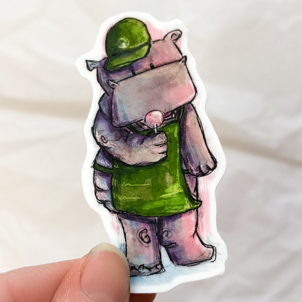 hippo wearing a green apron and hat with a cake pop in his hands.