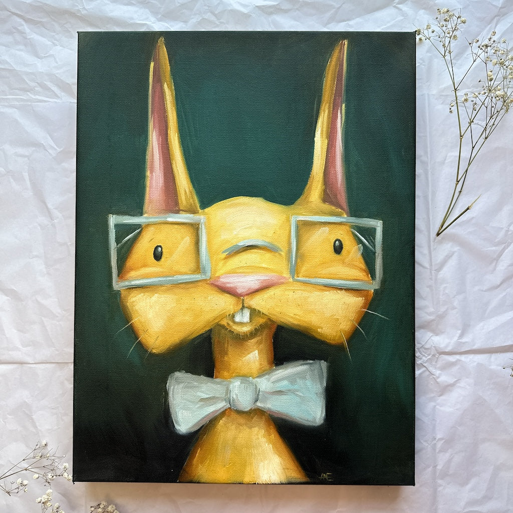 A golden yellow bunny with square glaseses on and wearing a pale blue bowtie.  The Bunny sits on a dark green background and his buck teeth are showing. 