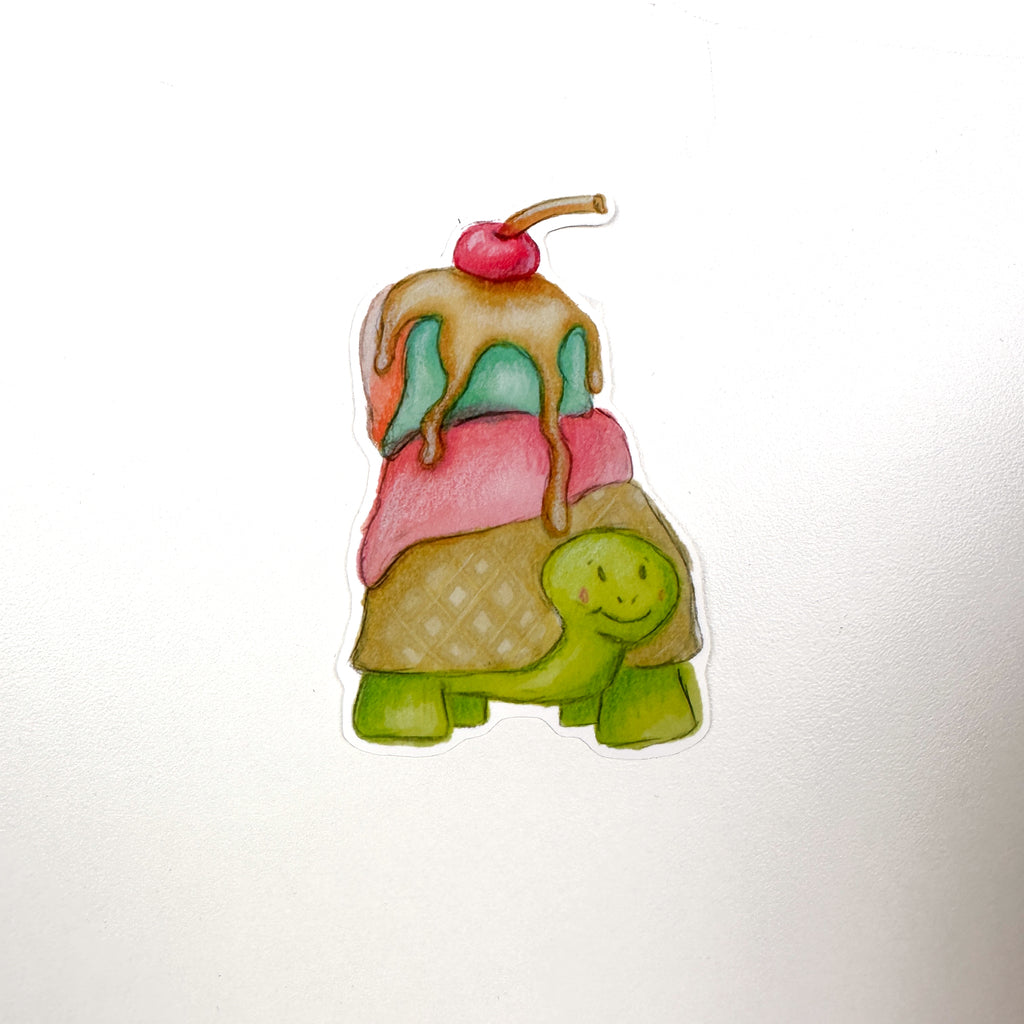 An illustrated sticker of a green turtle with a waffle cone shell and pink, blue and orange ice cream melting on top along with Carmel sauce dripping and a cherry on top!