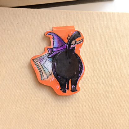 back of magnetic bookmark image of a black cat wearing a purple witches hat with a bat overhead and spellbook hovering in front of it. 
