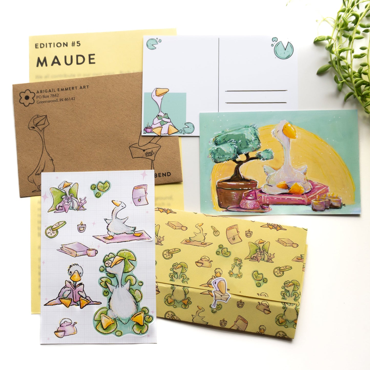 flat lay image of a happy mail bundle which has a sticker sheet with a goose reading, sleeping, doing yoga. A post card with a goose meditating, the back of a postcard with a goose reading. There is an envelope with a goose on it and a letter with goose pattern. 