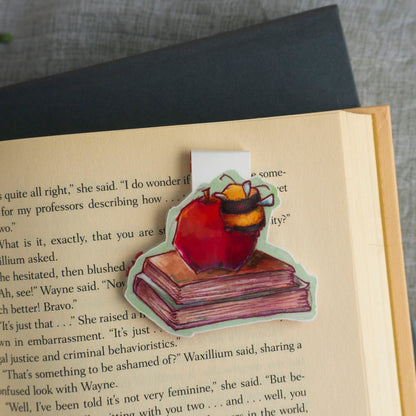 Open book with a sticker of a bee on a book and apple, placed on a textured surface.