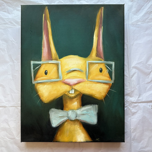 A golden yellow bunny with square glaseses on and wearing a pale blue bowtie.  The Bunny sits on a dark green background and his buck teeth are showing. 