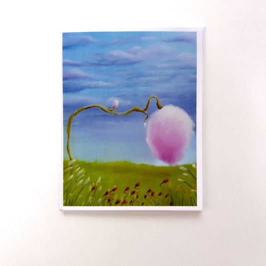 A whimsical and surreal illustrative style painting of a tree with cotton candy instead of leaves positioned in a field with blue and lavender colored skies. This photo depicts this artwork on the greeting card with the card envelope tucked behind it.