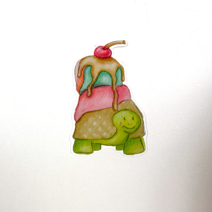An illustrated sticker of a green turtle with a waffle cone shell and pink, blue and orange ice cream melting on top along with Carmel sauce dripping and a cherry on top!