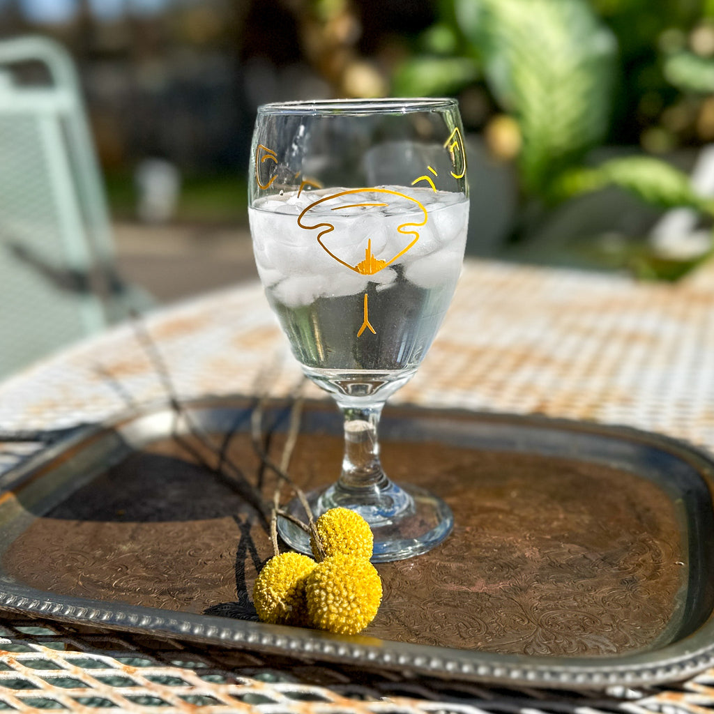 iced tea glass with yellow outline of a bear face on the front in an outside setting. The glass has ice water in it. 